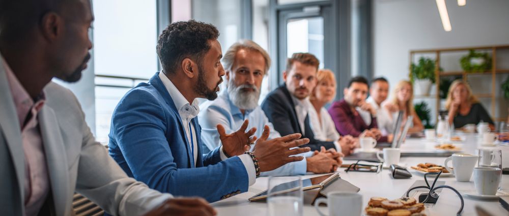 Determined African businessman expressing opinions to junior and senior colleagues on management team in conference room.