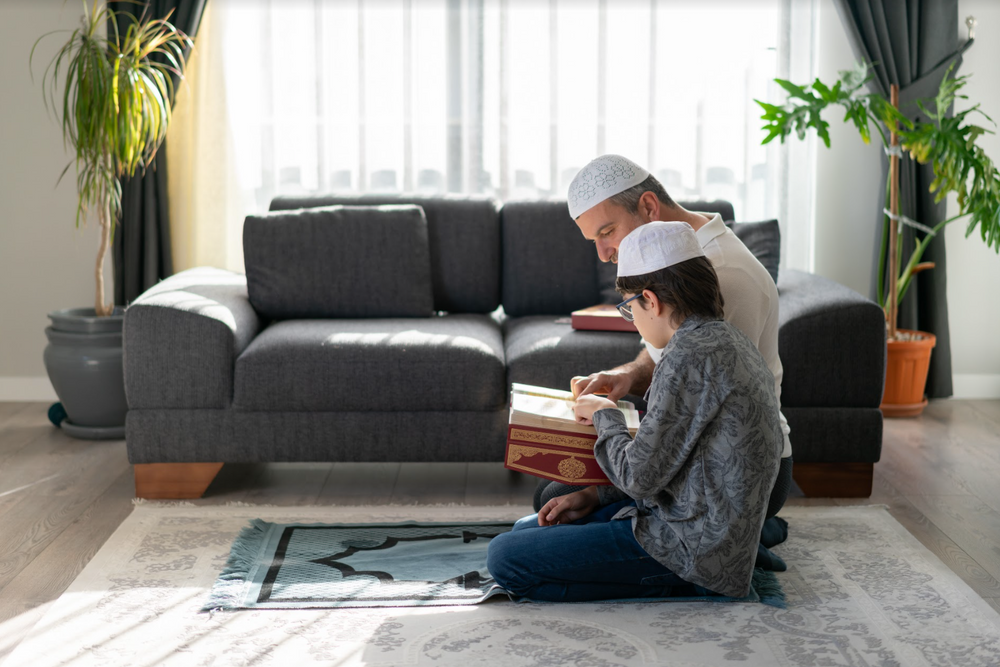Son and father reading Quran together at home stock photo