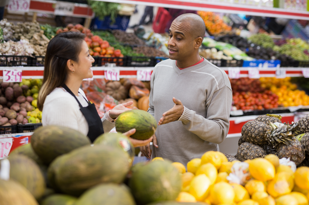Latinx man in fruit section of supermarket with shop worker helping him