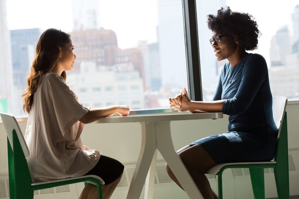 a Black women and a white woman sitting across a table from each other in a job interview