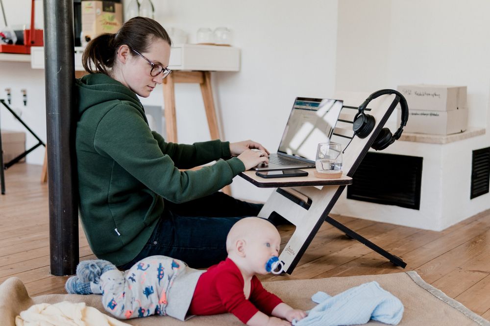 Mother working from home on a laptop while watching her toddler beside her