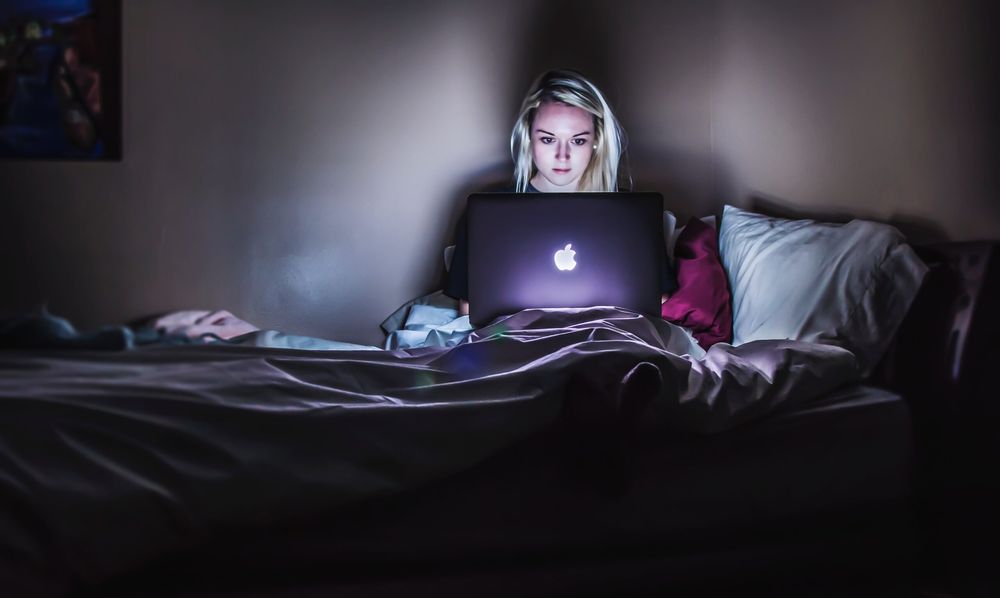 Woman sitting in the dark in bed, working on a laptop with headphones on
