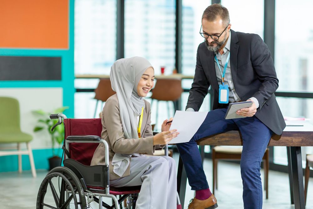 Asian Muslim businesswoman sitting on wheelchair presenting business graph on paper to manager. 