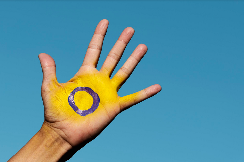 Intersex symbol of a purple circle on a yellow background painted on an open hand