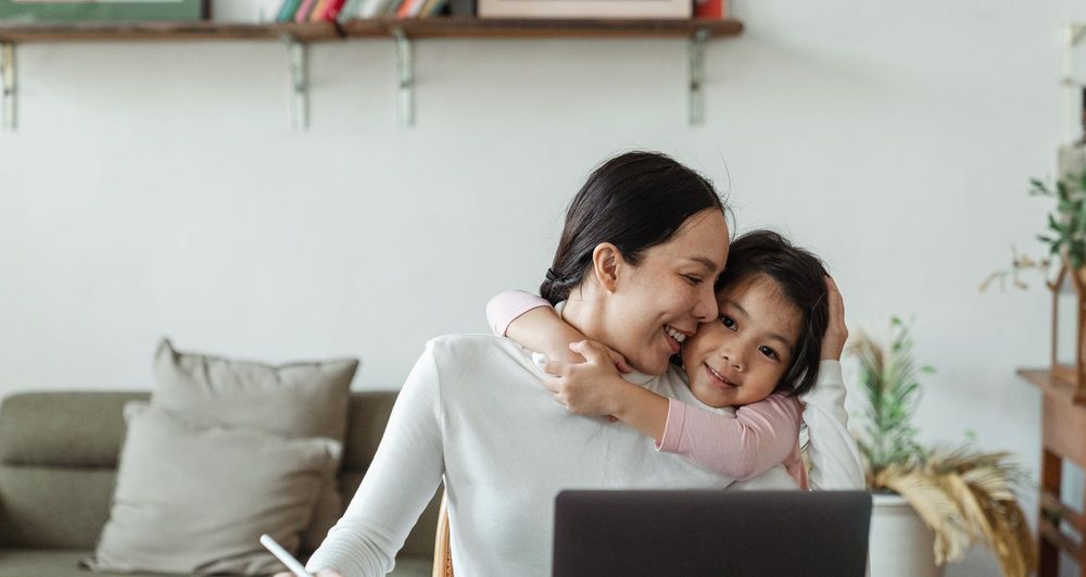 Parent hugs a child in front of a work-from-home laptop
