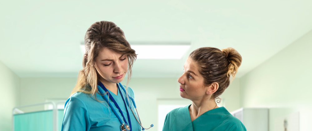 A younger nurse and an older nurse discuss a patient chart
