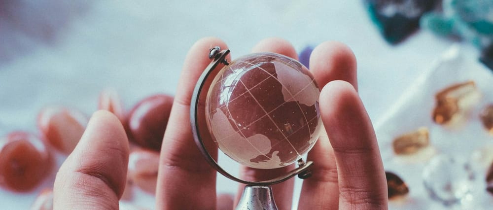 A pale skinned hand holding a glass globe figurine