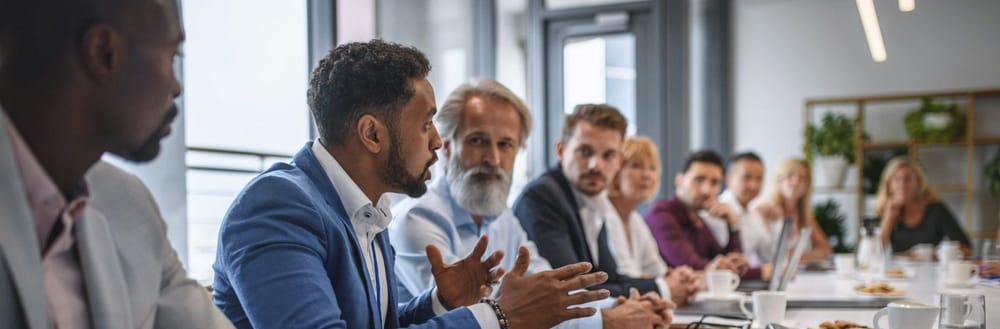 Determined African businessman expressing opinions to junior and senior colleagues on management team in conference room.