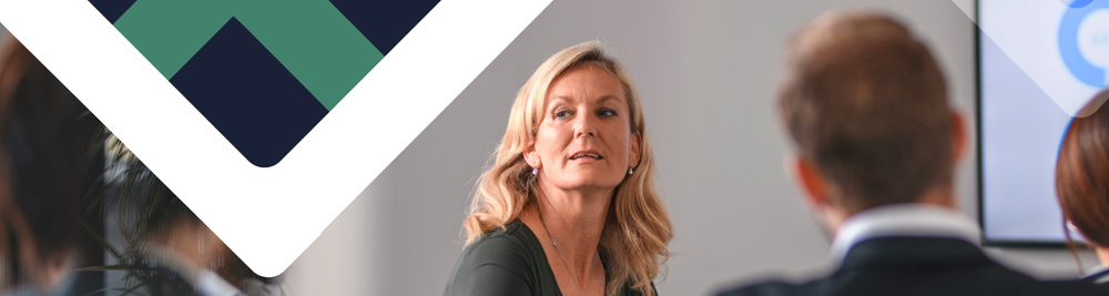 Picture of a White woman with blond hair sitting at a conference table