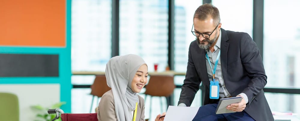 Asian Muslim businesswoman sitting on wheelchair presenting business graph on paper to manager. 