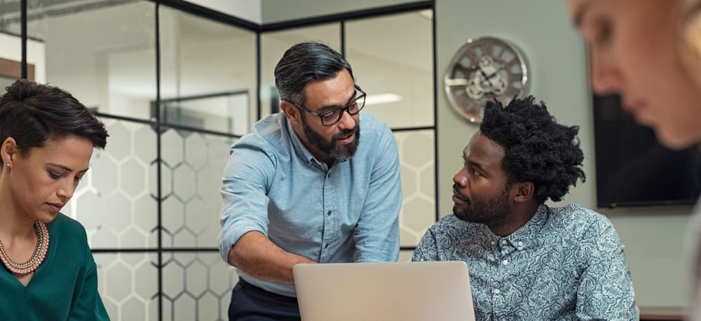 Latin mature manager discussing with his colleague online data in front of laptop. 