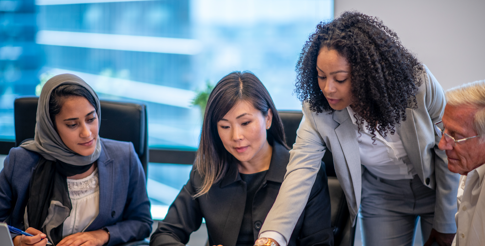 A group of diverse businesspeople are having a meeting in an office gathered around a table to look at documents.