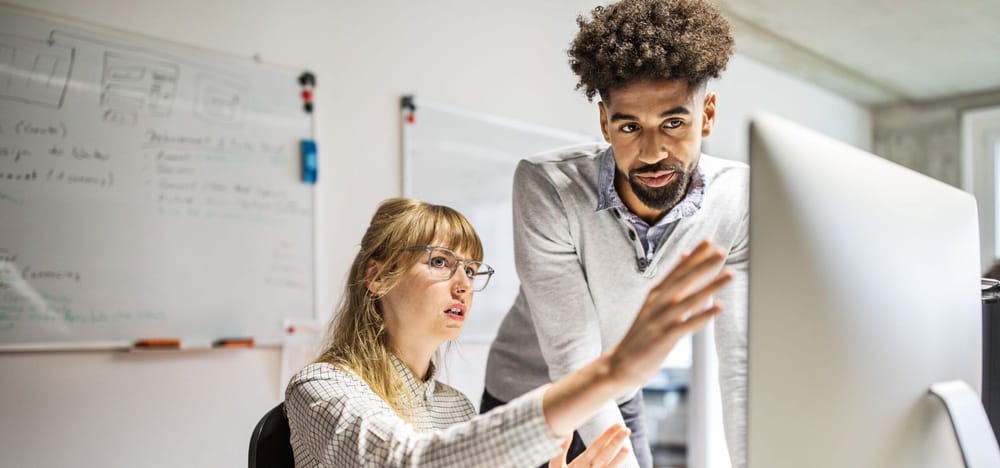 Multi-ethnic businesswoman and businessman discussing over computer at desk in creative office