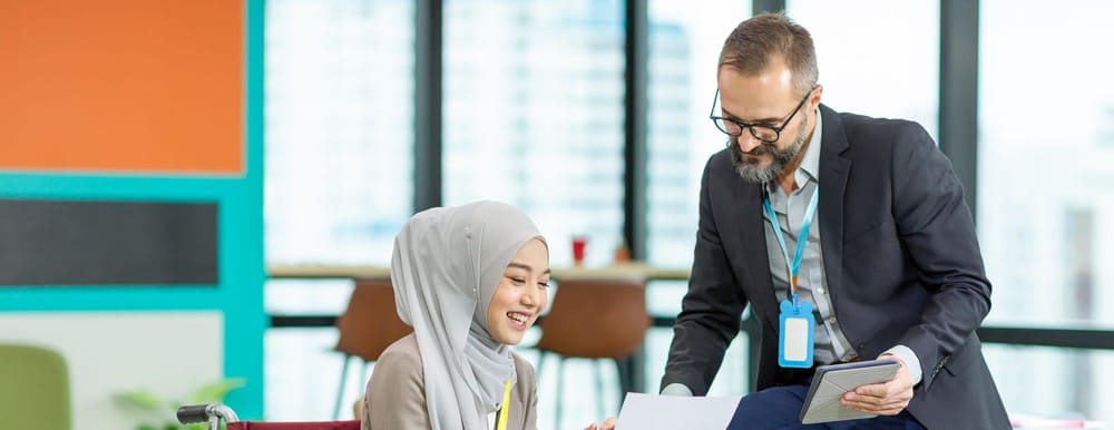 Asian Muslim businesswoman sitting on wheelchair presenting business graph on paper to manager. 