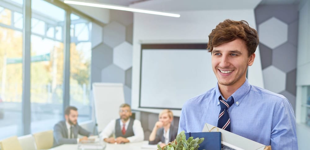 A man carrying a box smiles while exiting his offboarding meeting