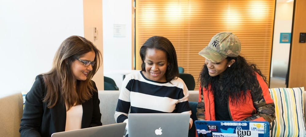 Three women sitting on a couch with laptops